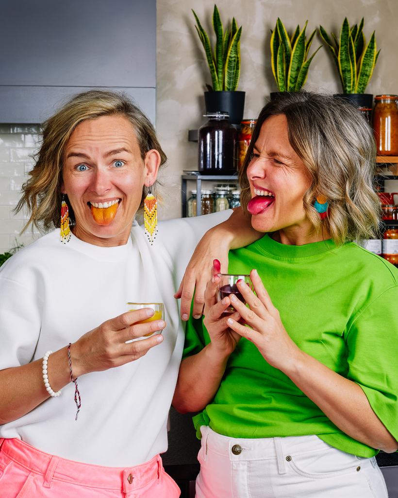Marta en Joanna Klejman met hun tong uit de mond, elk met een gefermenteerd drankje in de hand