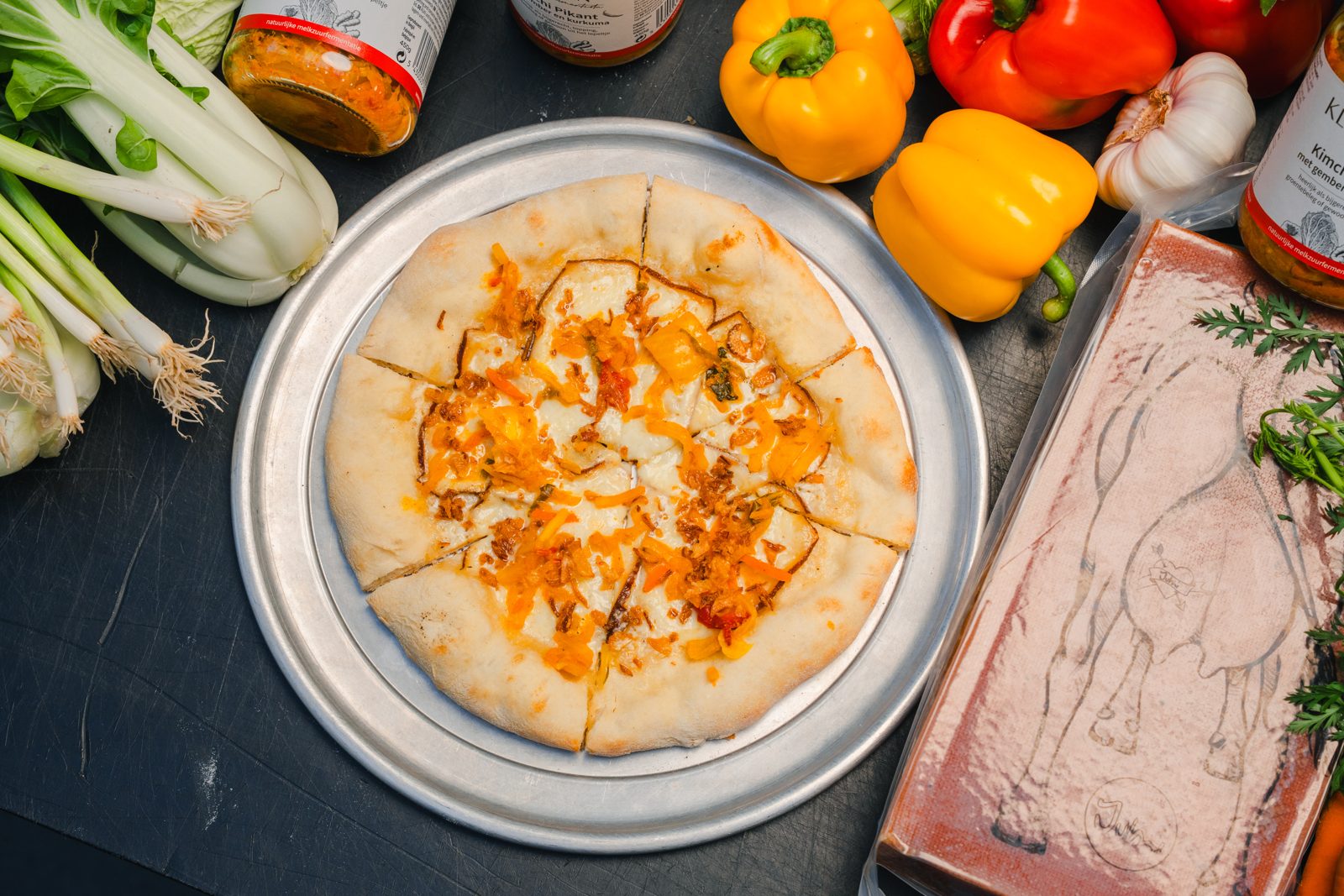 De Cheesy Kimchi-pizza van Otomat met gerookte raclette en kimchi, omringd door verse groenten