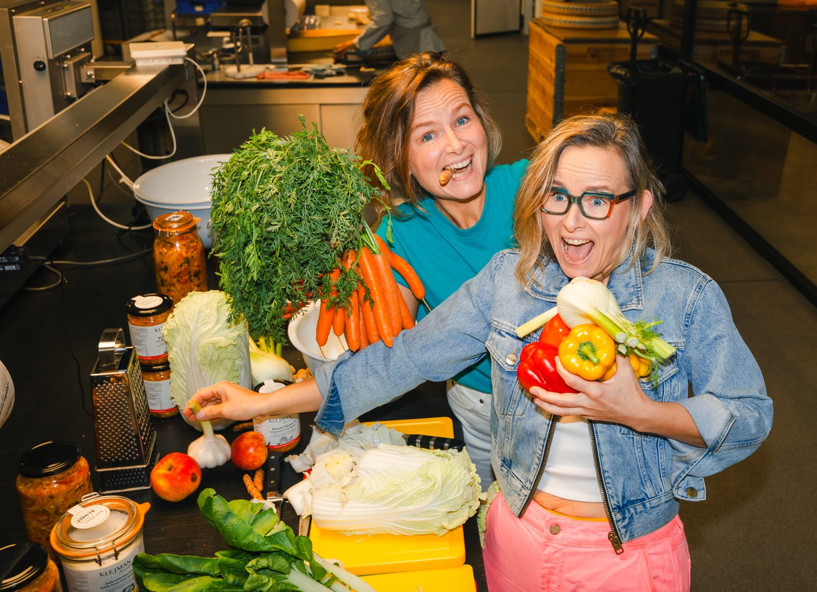 Marta en Joanna Klejman lachend in de keuken met wortels, paprika's, venkel en Chinese kool