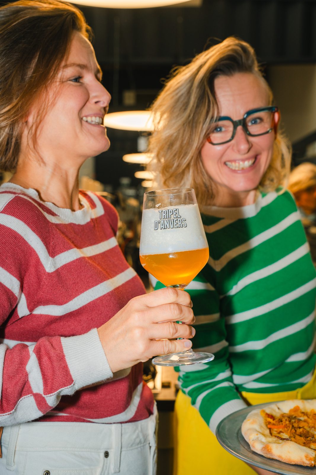 De zusjes Klejman lachend met een glas bier en een pizza